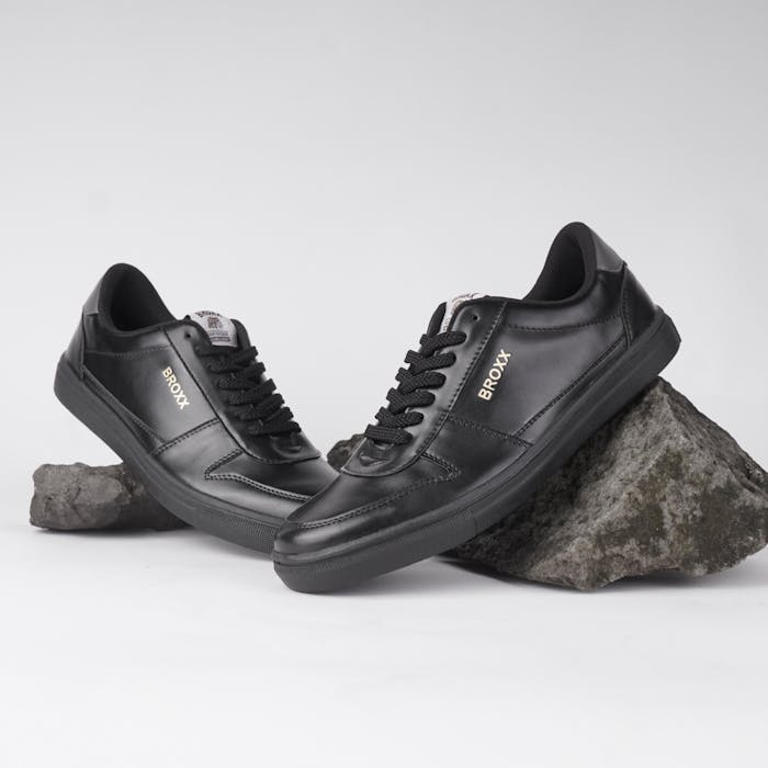 our-story Stylish black sneakers posed elegantly on rocks, showcasing contemporary fashion footwear.