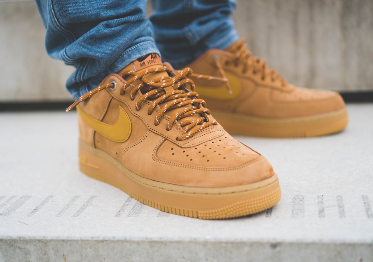 Stylish brown Nike Air Force 1 sneakers paired with blue jeans on a concrete surface.
