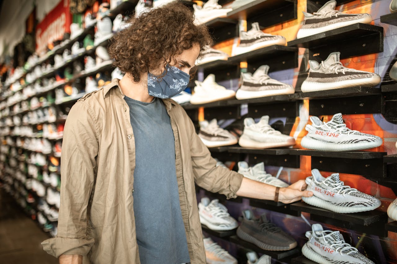 Man shopping for trendy Adidas Yeezy sneakers, wearing a mask in a stylish footwear store.